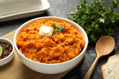 Photo of Delicious mashed sweet potatoes with butter, spices, bread and spoon on dark table, closeup