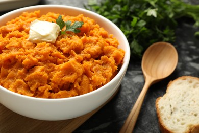 Photo of Delicious mashed sweet potatoes with butter, parsley, bread and spoon on dark table, closeup