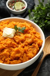 Delicious mashed sweet potatoes with butter, parsley, bread and spoon on dark table, closeup