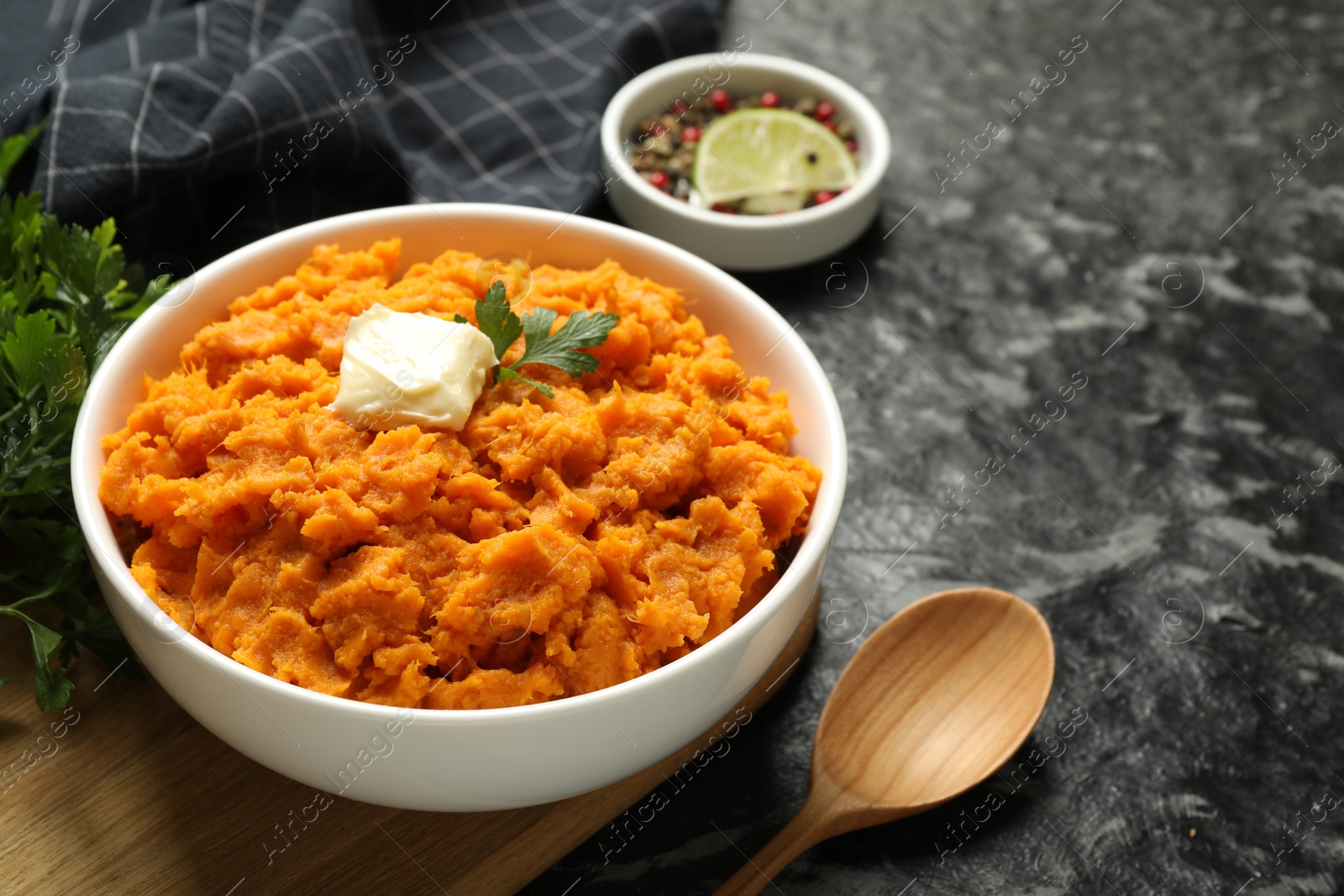 Photo of Delicious mashed sweet potatoes with butter, spices and spoon on dark table, closeup