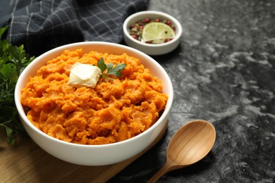 Photo of Delicious mashed sweet potatoes with butter, spices and spoon on dark table, closeup