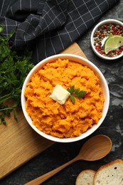 Photo of Delicious mashed sweet potatoes with butter, spices, bread and spoon on dark table, top view