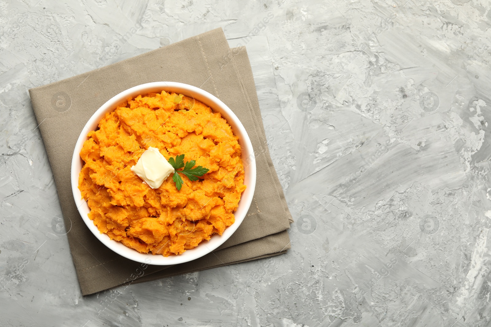 Photo of Delicious mashed sweet potatoes with butter and parsley in bowl on grey table, top view. Space for text