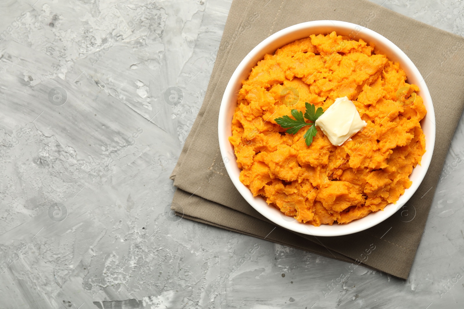 Photo of Delicious mashed sweet potatoes with butter and parsley in bowl on grey table, top view. Space for text