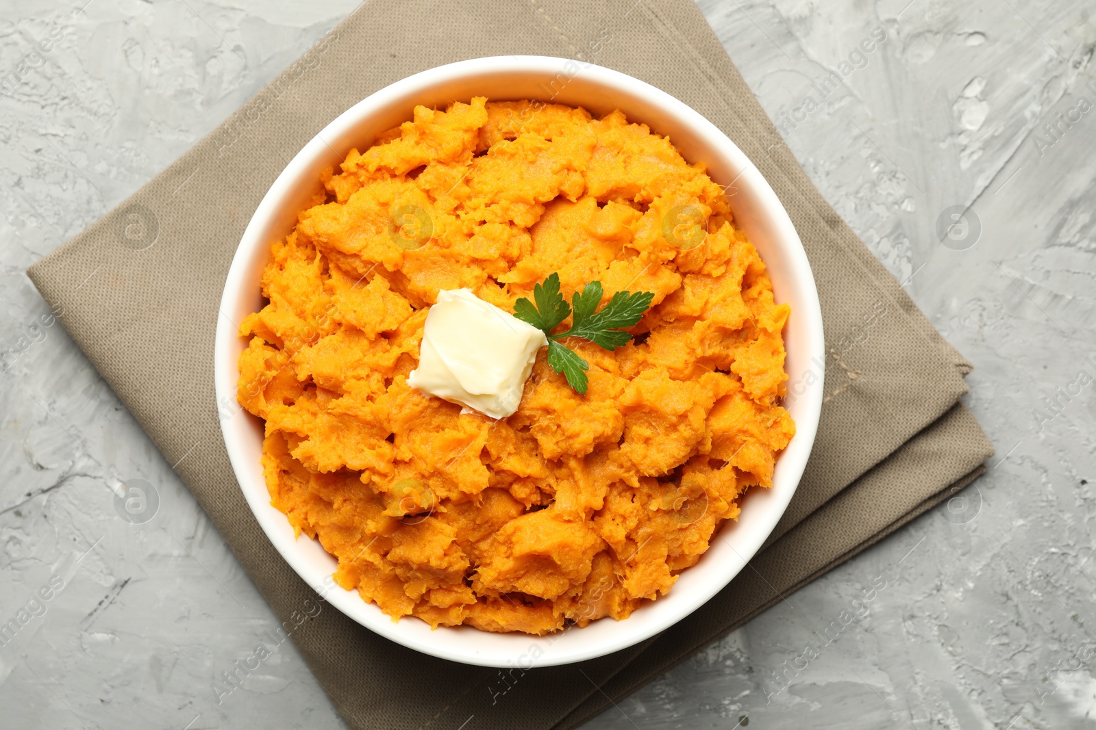 Photo of Delicious mashed sweet potatoes with butter and parsley in bowl on grey table, top view