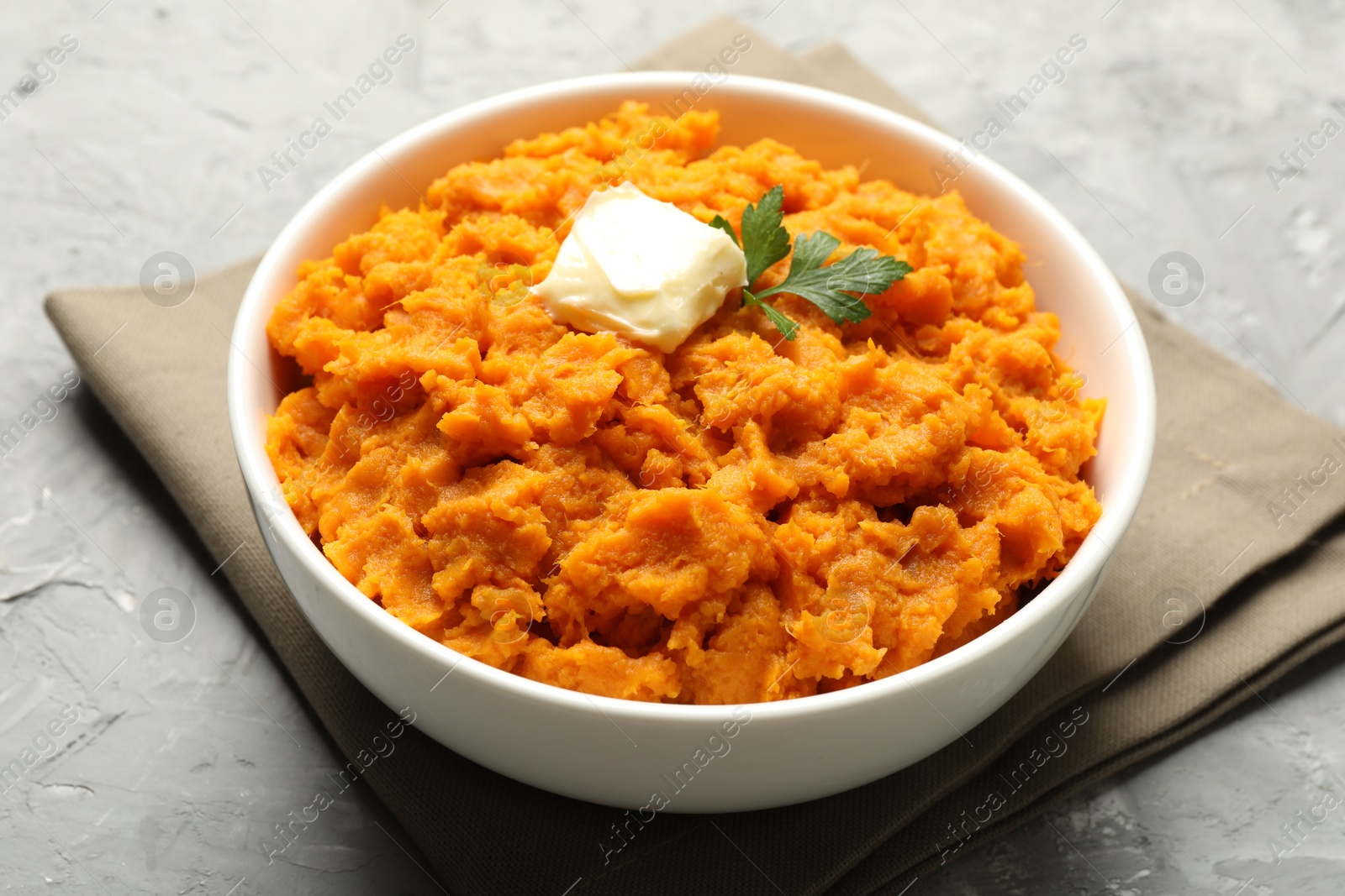 Photo of Delicious mashed sweet potatoes with butter and parsley in bowl on grey table, closeup