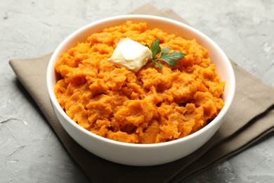 Photo of Delicious mashed sweet potatoes with butter and parsley in bowl on grey table, closeup