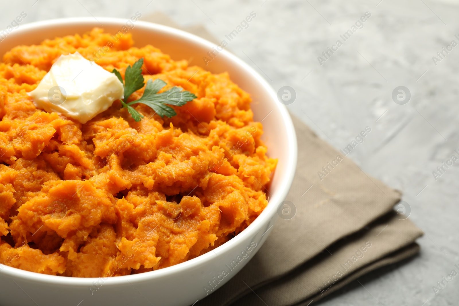 Photo of Delicious mashed sweet potatoes with butter and parsley in bowl on grey table, closeup