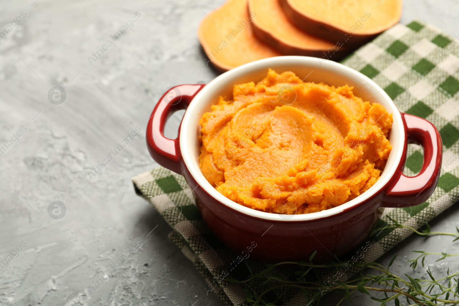 Photo of Delicious mashed sweet potatoes in pot, vegetable and microgreens on grey table, closeup