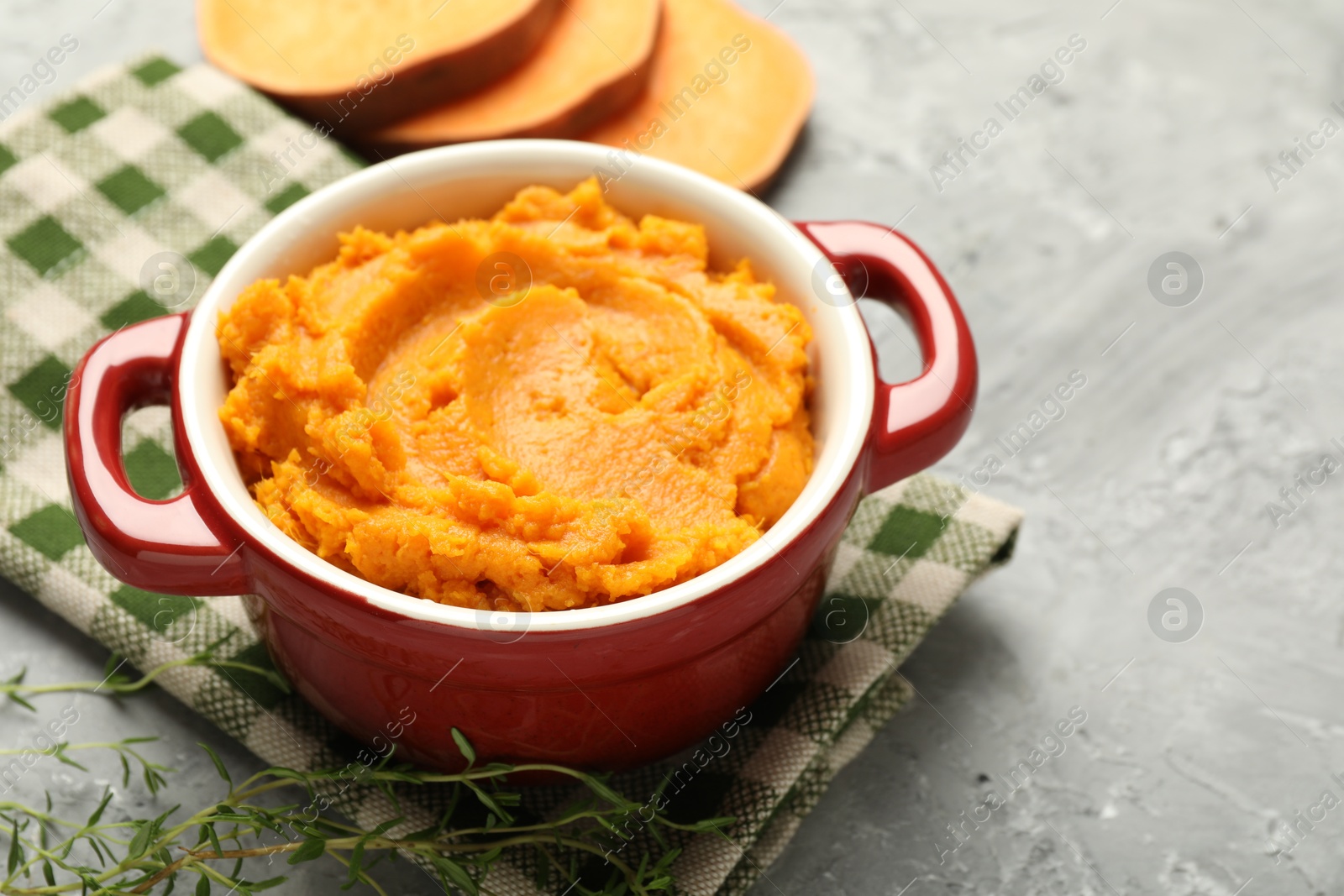 Photo of Delicious mashed sweet potatoes in pot, vegetable and microgreens on grey table, closeup