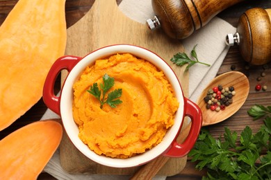 Photo of Delicious mashed sweet potatoes in pot, vegetable, parsley and spices on wooden table, top view