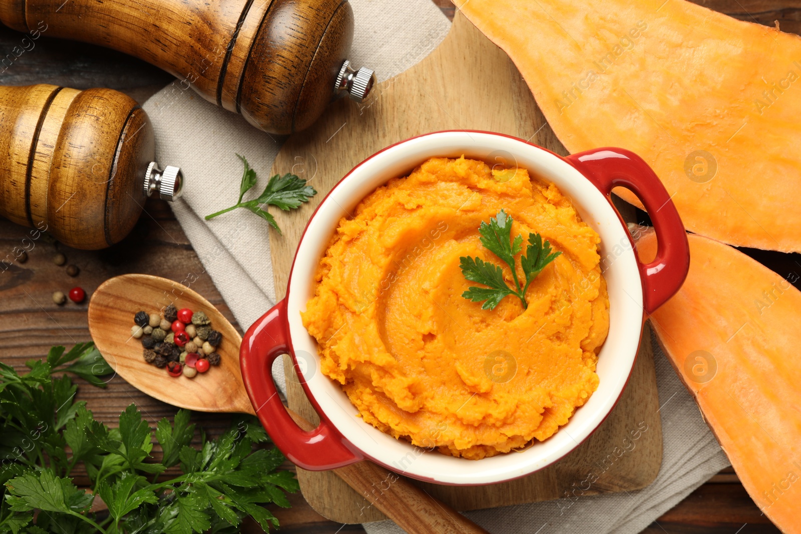 Photo of Delicious mashed sweet potatoes in pot, vegetable, parsley and spices on wooden table, top view