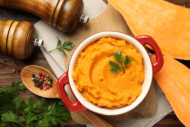 Delicious mashed sweet potatoes in pot, vegetable, parsley and spices on wooden table, top view