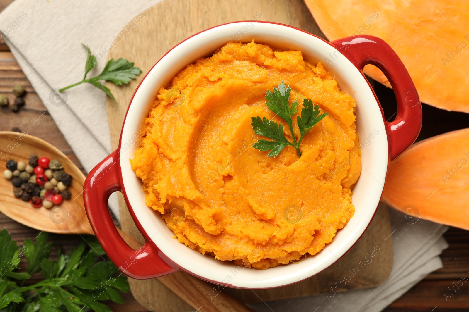 Photo of Delicious mashed sweet potatoes in pot, vegetable, parsley and spices on wooden table, top view