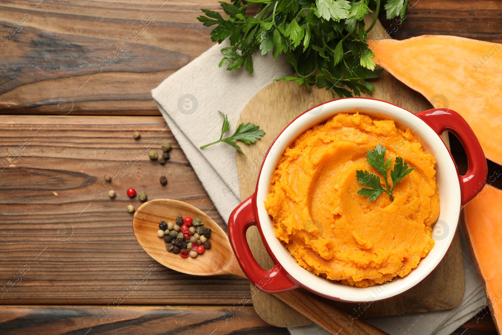 Photo of Delicious mashed sweet potatoes in pot, vegetable, parsley and spices on wooden table, top view