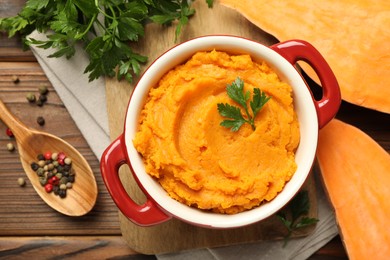 Delicious mashed sweet potatoes in pot, vegetable, parsley and spices on wooden table, top view