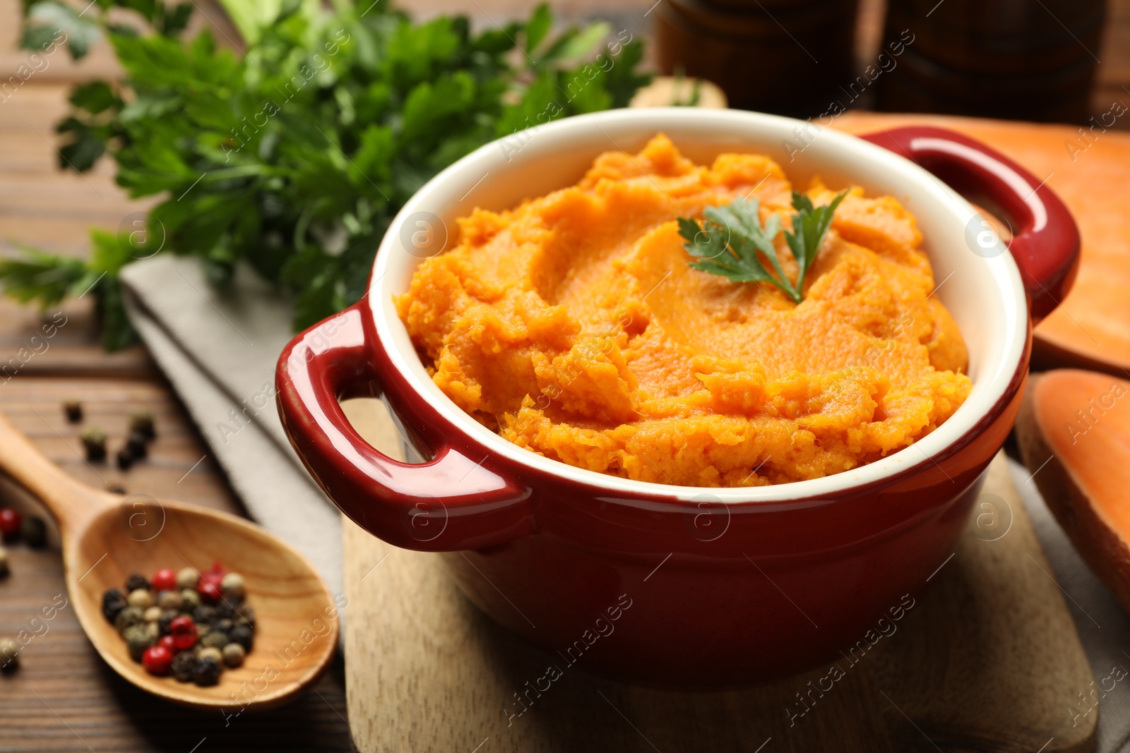 Photo of Delicious mashed sweet potatoes in pot and spices on wooden table, closeup