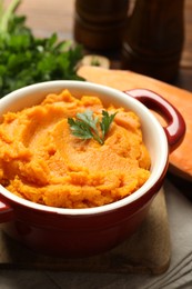 Delicious mashed sweet potatoes in pot and parsley on table, closeup