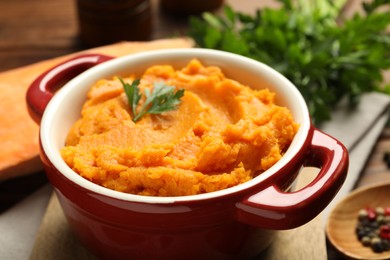 Delicious mashed sweet potatoes in pot and parsley on table, closeup