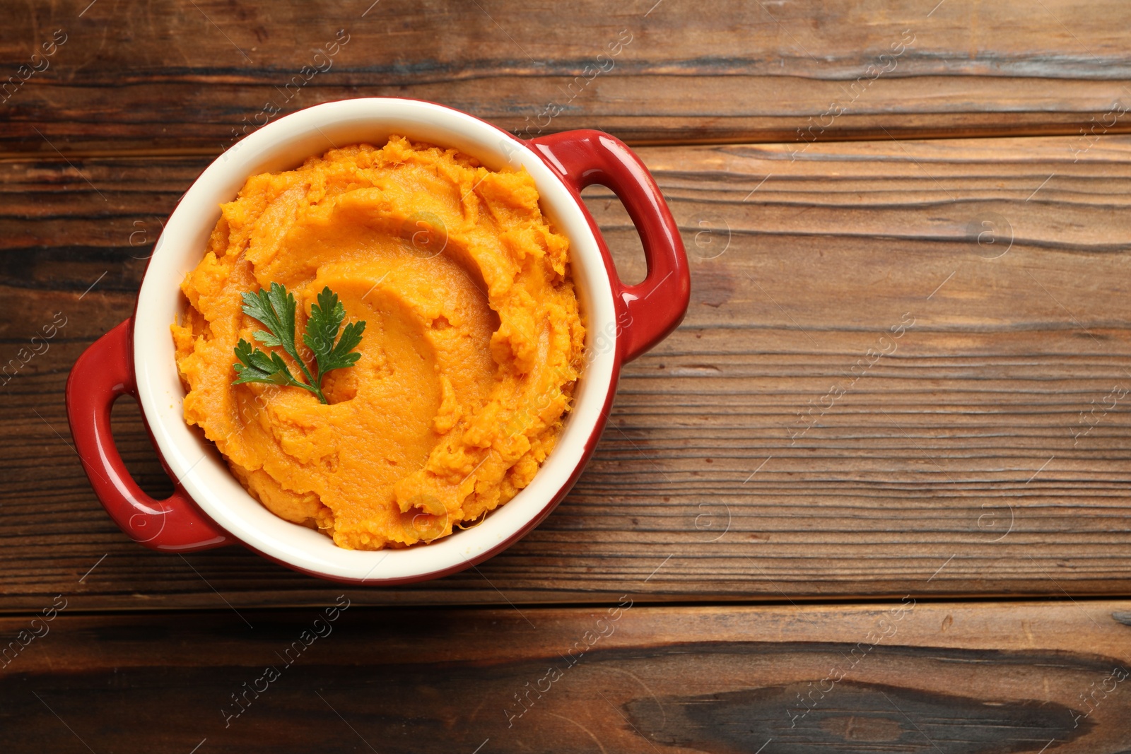 Photo of Delicious mashed sweet potatoes with parsley in pot on wooden table, top view. Space for text