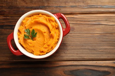 Delicious mashed sweet potatoes with parsley in pot on wooden table, top view. Space for text