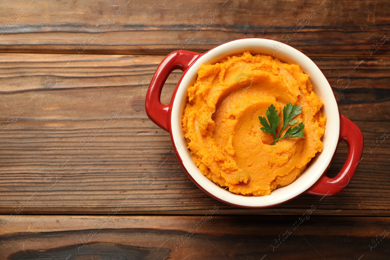 Photo of Delicious mashed sweet potatoes with parsley in pot on wooden table, top view. Space for text