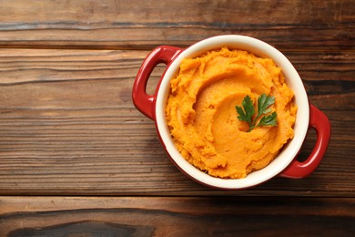 Photo of Delicious mashed sweet potatoes with parsley in pot on wooden table, top view. Space for text