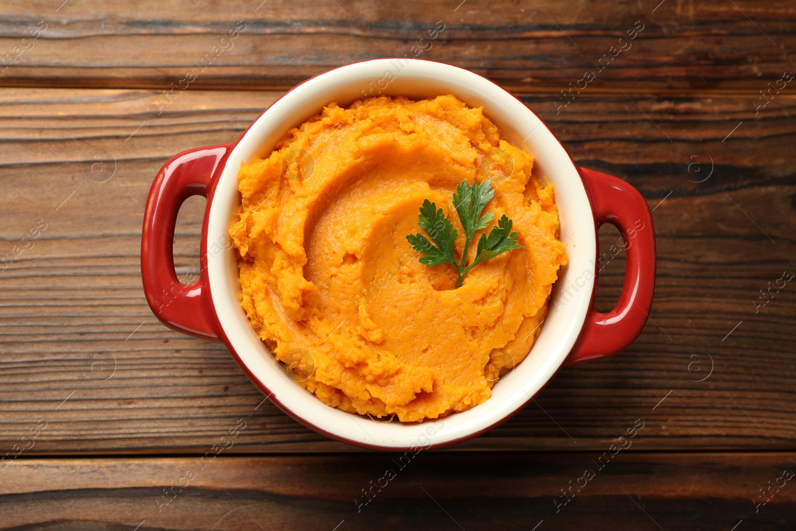 Photo of Delicious mashed sweet potatoes with parsley in pot on wooden table, top view