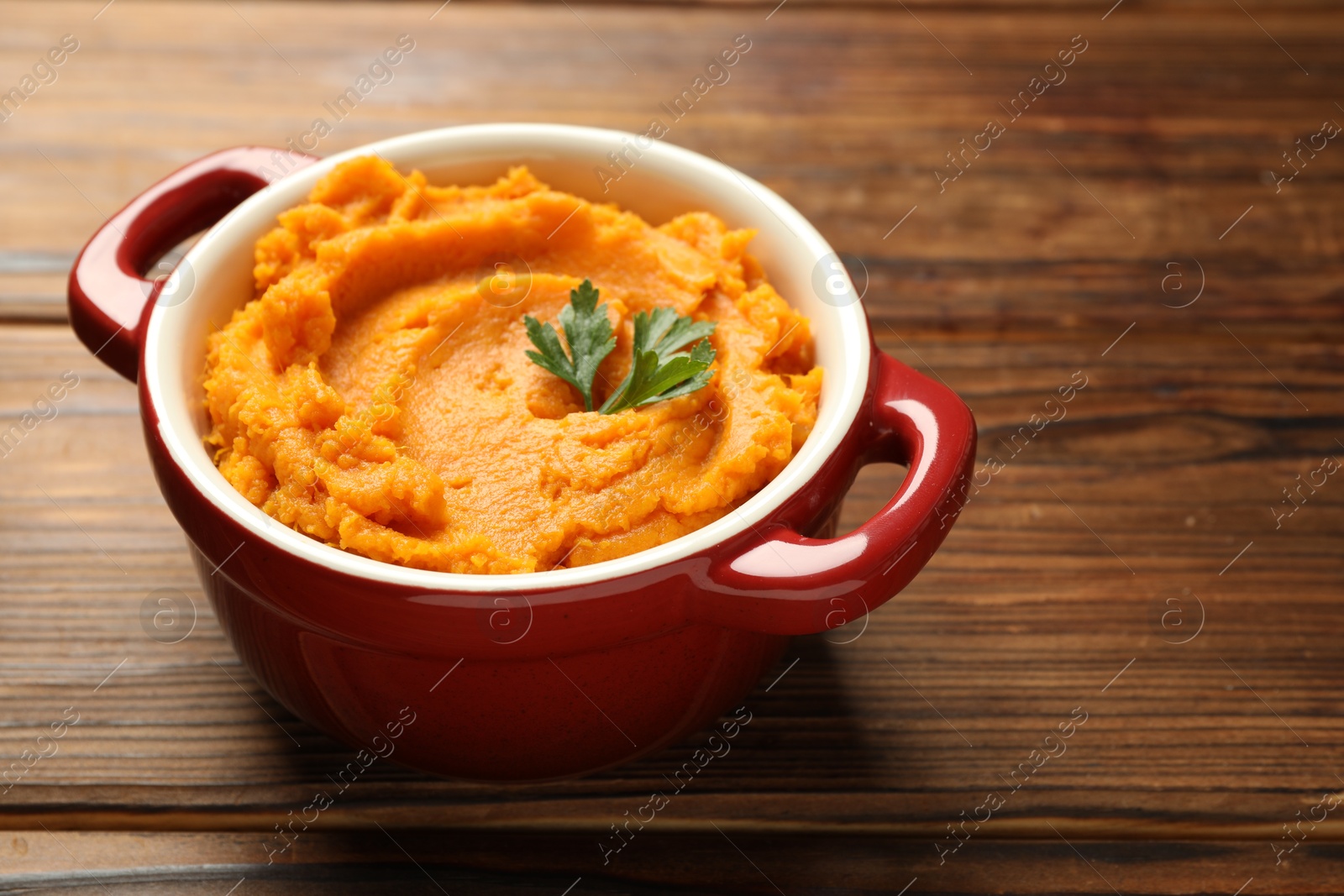 Photo of Delicious mashed sweet potatoes with parsley in pot on wooden table, closeup