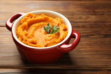 Photo of Delicious mashed sweet potatoes with parsley in pot on wooden table, closeup