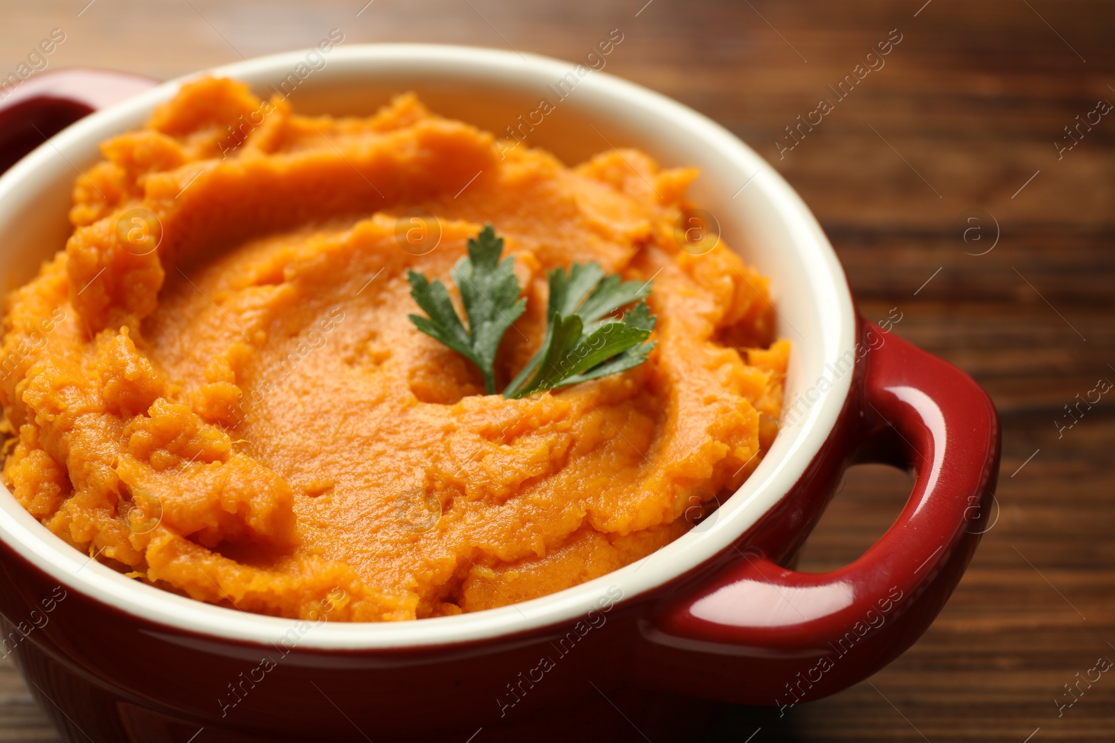 Photo of Delicious mashed sweet potatoes with parsley in pot on wooden table, closeup