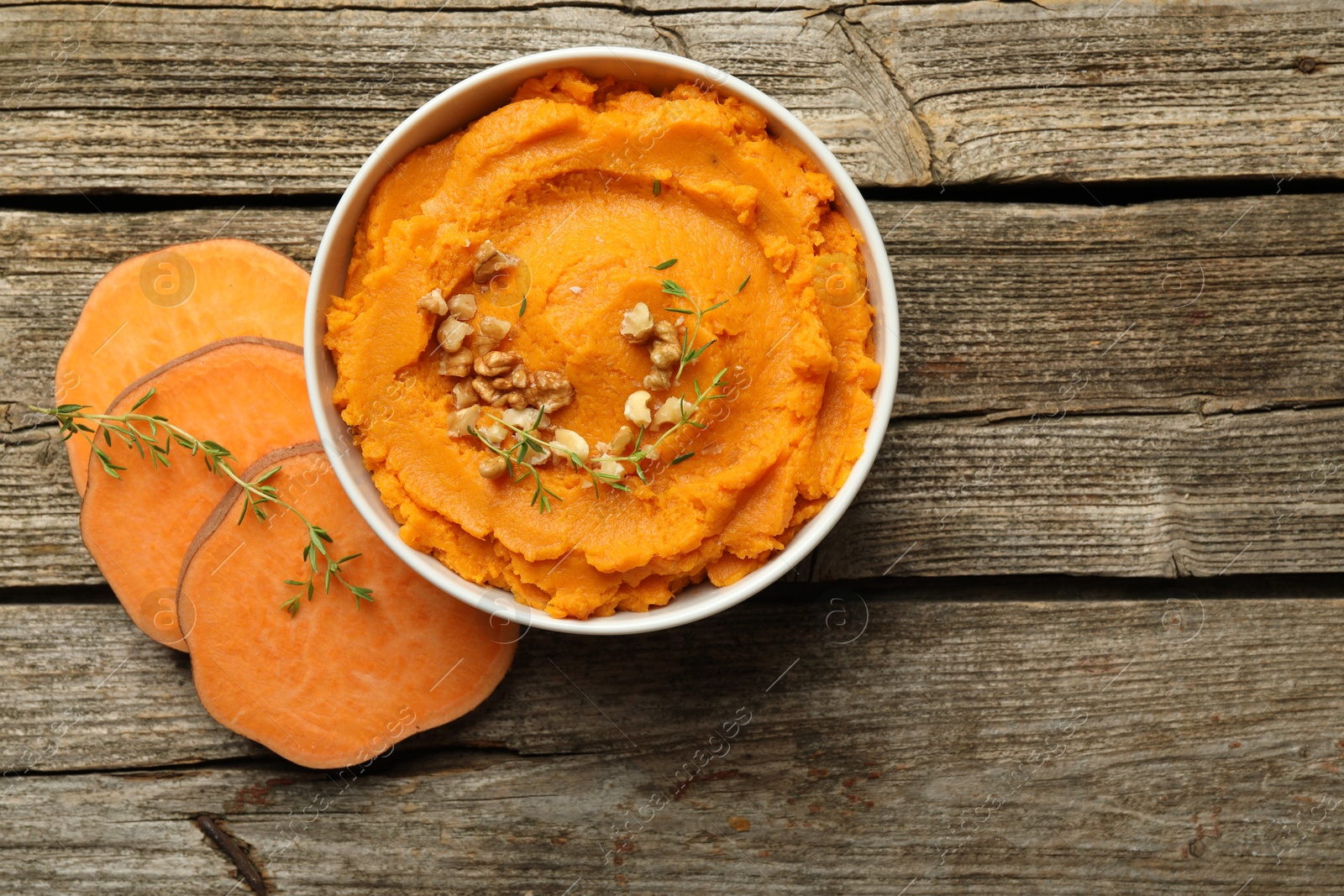 Photo of Delicious mashed sweet potatoes in bowl, walnuts and cut vegetable on wooden table, top view. Space for text