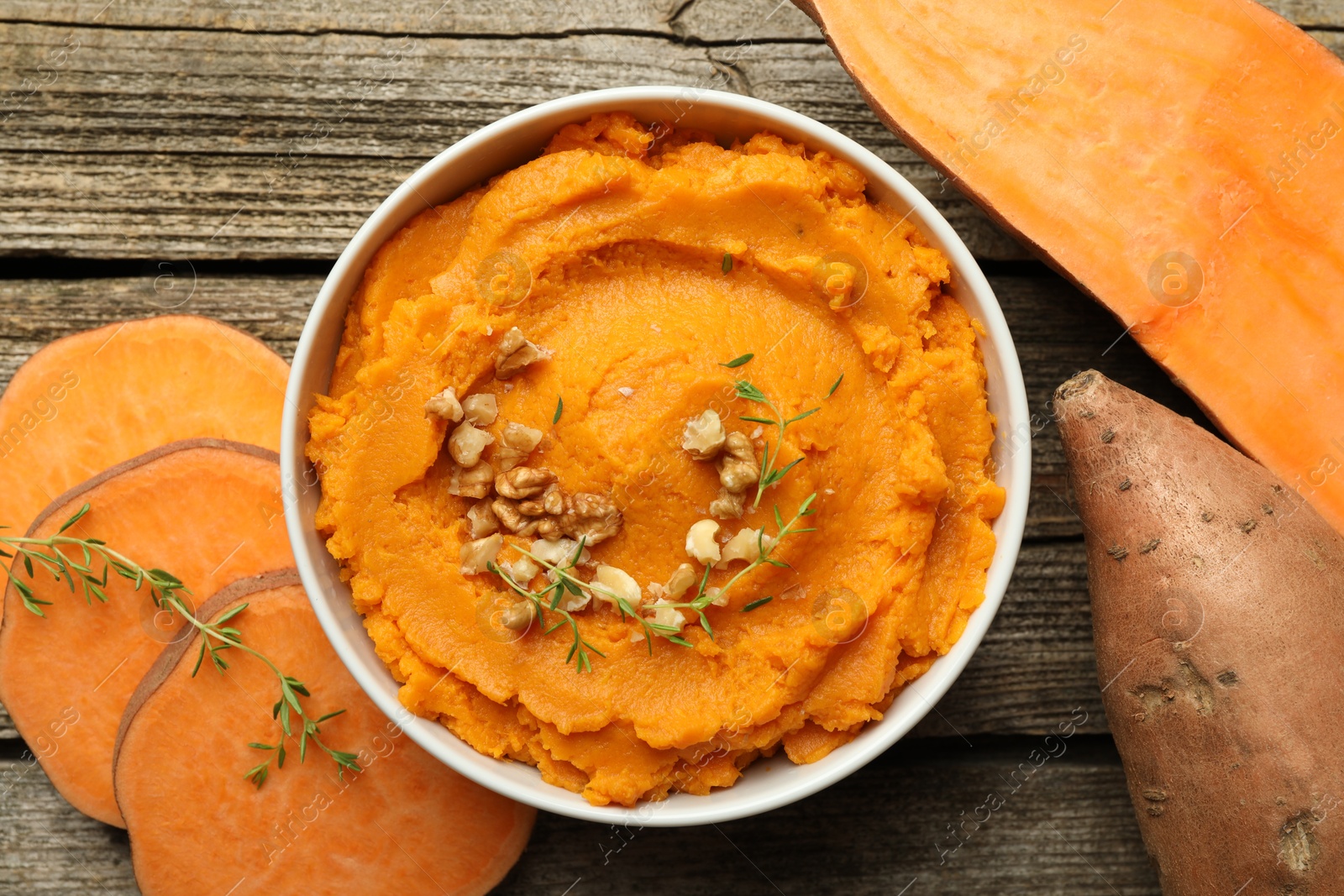 Photo of Delicious mashed sweet potatoes in bowl, walnuts and vegetables on wooden table, top view