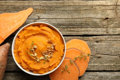 Delicious mashed sweet potatoes in bowl, walnuts and vegetables on wooden table, top view