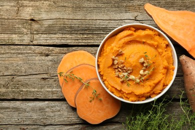 Photo of Delicious mashed sweet potatoes in bowl, walnuts and vegetables on wooden table, top view. Space for text