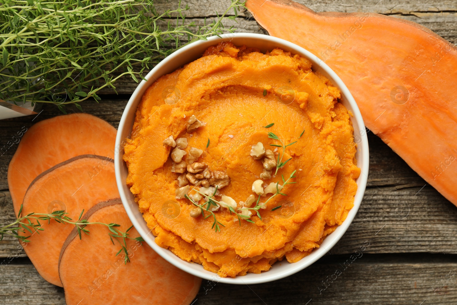 Photo of Delicious mashed sweet potatoes with nuts in bowl, vegetables and microgreens on wooden table, top view