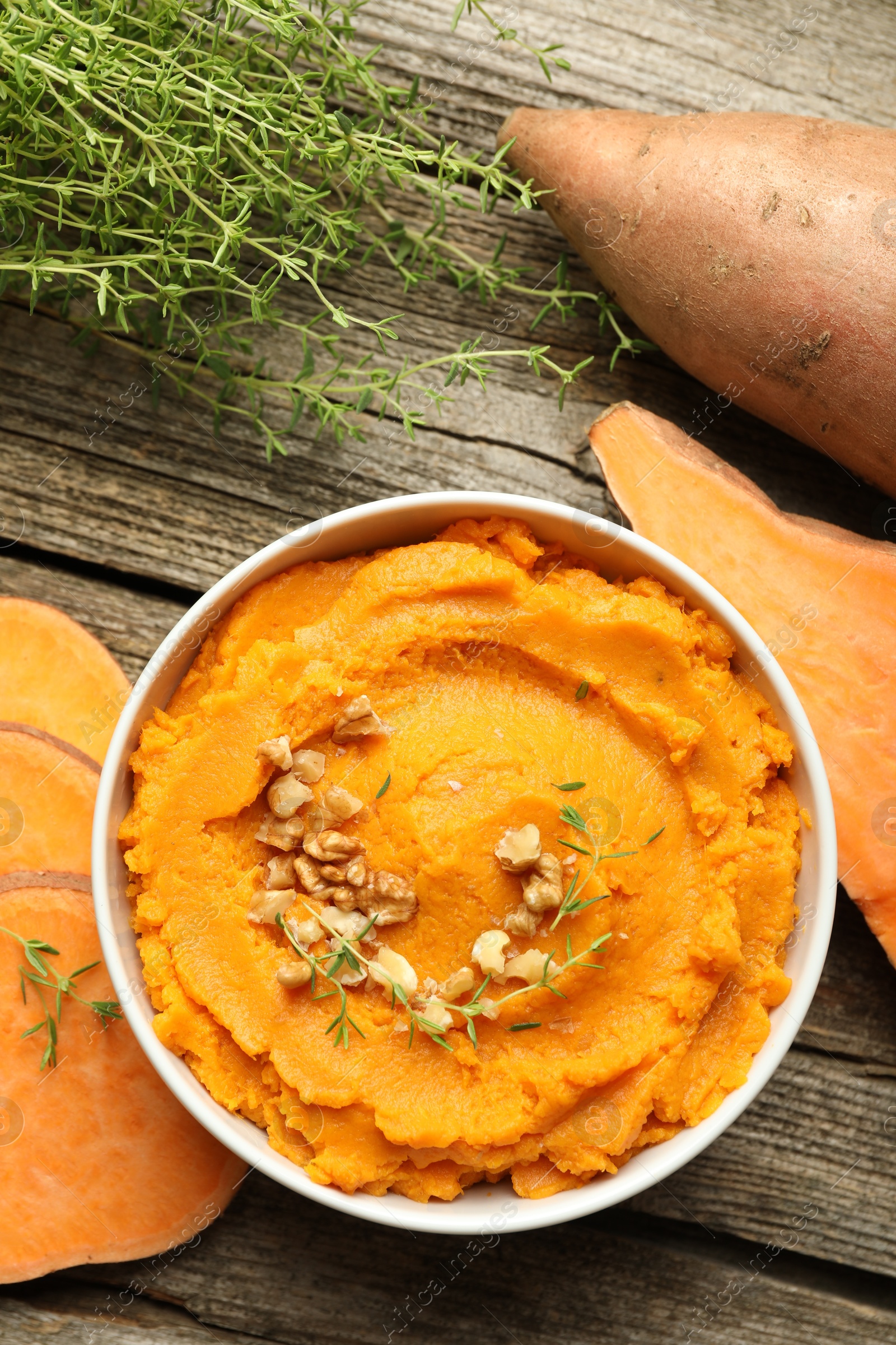 Photo of Delicious mashed sweet potatoes with nuts in bowl, vegetables and microgreens on wooden table, top view