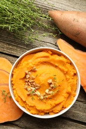 Delicious mashed sweet potatoes with nuts in bowl, vegetables and microgreens on wooden table, top view