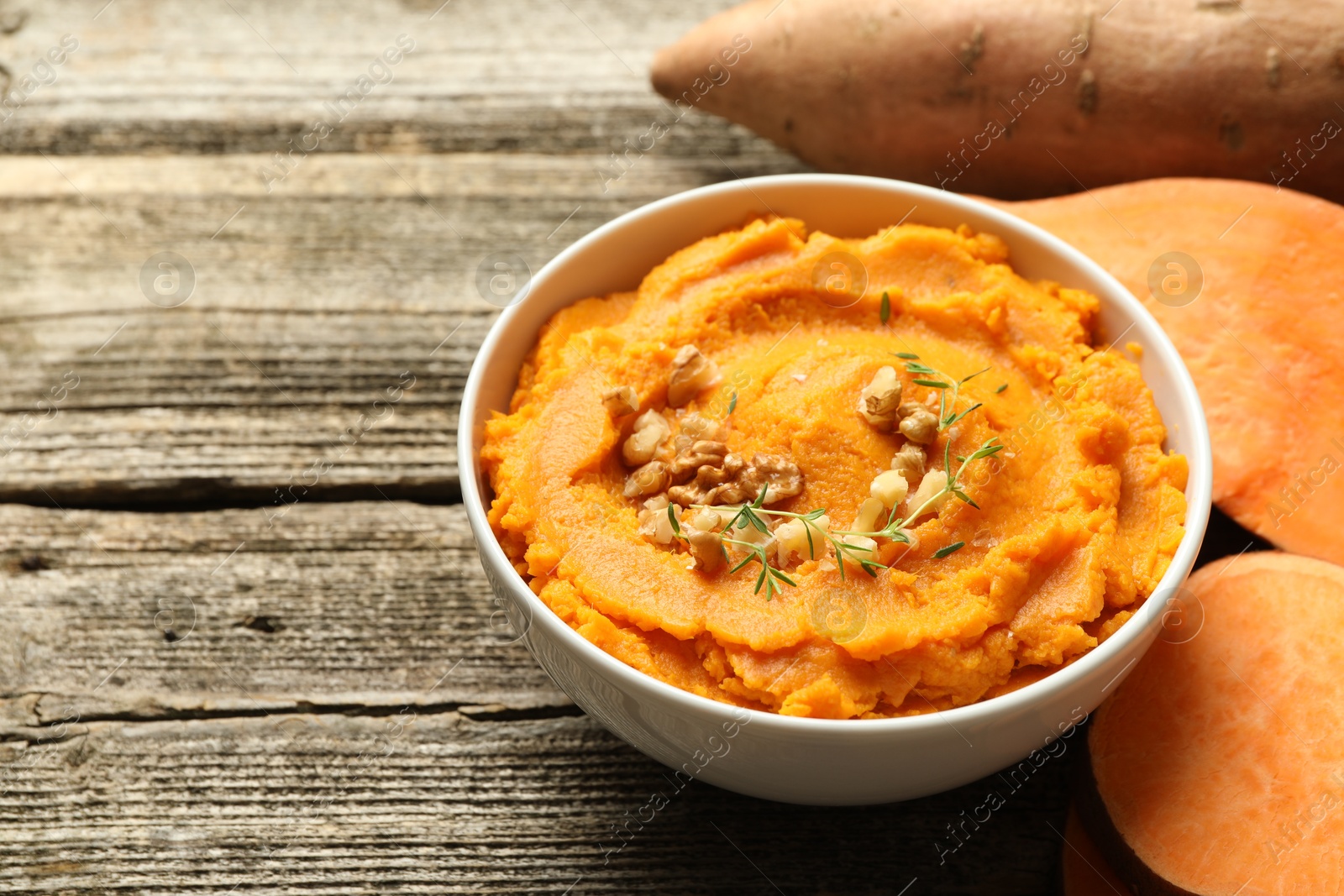 Photo of Delicious mashed sweet potatoes in bowl and vegetables on wooden table, closeup. Space for text