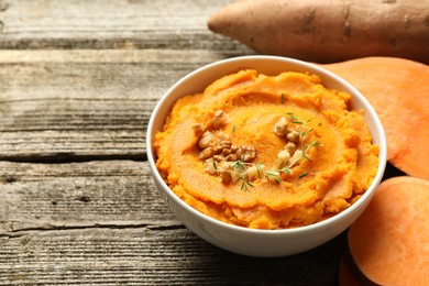 Delicious mashed sweet potatoes in bowl and vegetables on wooden table, closeup. Space for text