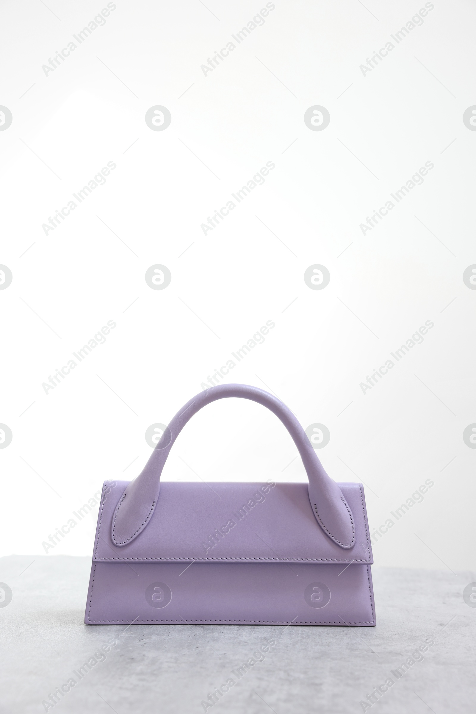 Photo of Stylish violet bag on gray table against light background, space for text