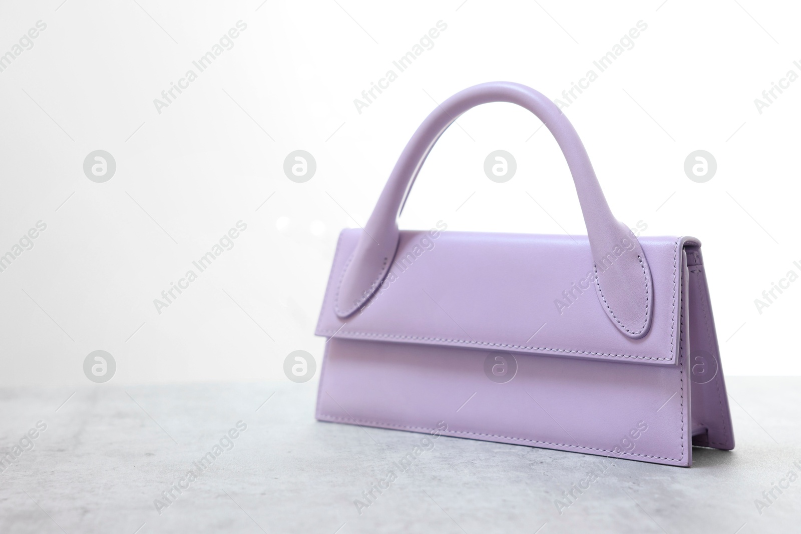 Photo of Stylish violet bag on gray table against light background, space for text