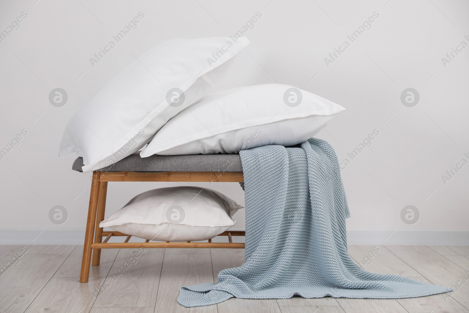 Photo of Clean pillows, blanket and storage bench on floor near white wall