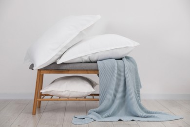 Clean pillows, blanket and storage bench on floor near white wall