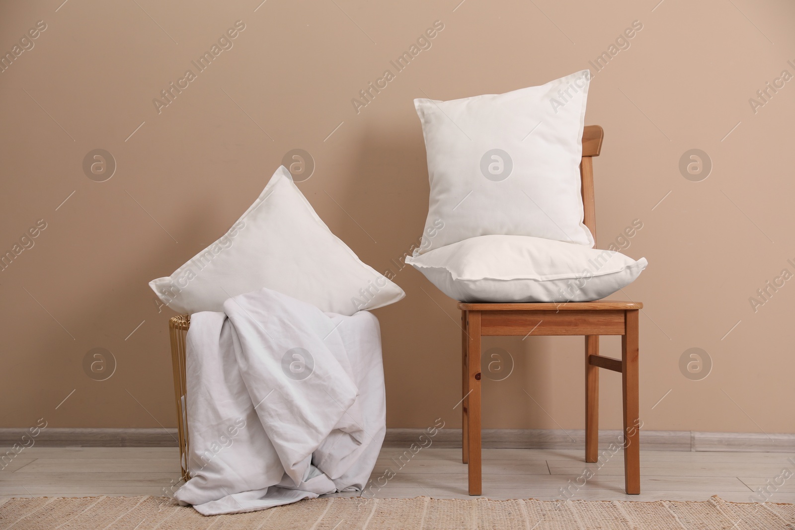 Photo of White pillows, chair, storage basket and blanket near beige wall