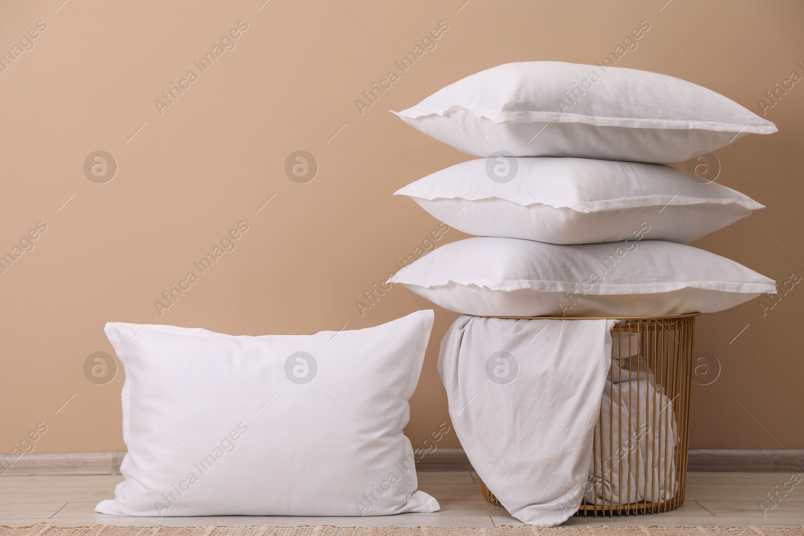 Photo of White pillows, storage basket and blanket near beige wall