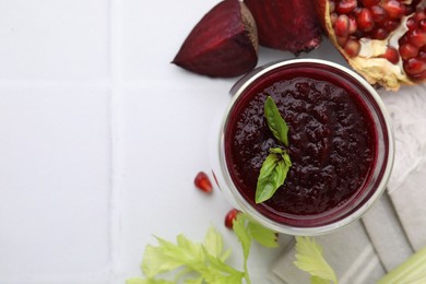 Photo of Fresh beetroot smoothie with mint, beet and pomegranate on white tiled table, flat lay. Space for text