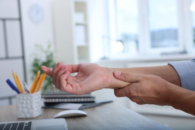 Photo of Man suffering from pain in wrist while working on laptop at table indoors, closeup. Carpal tunnel syndrome