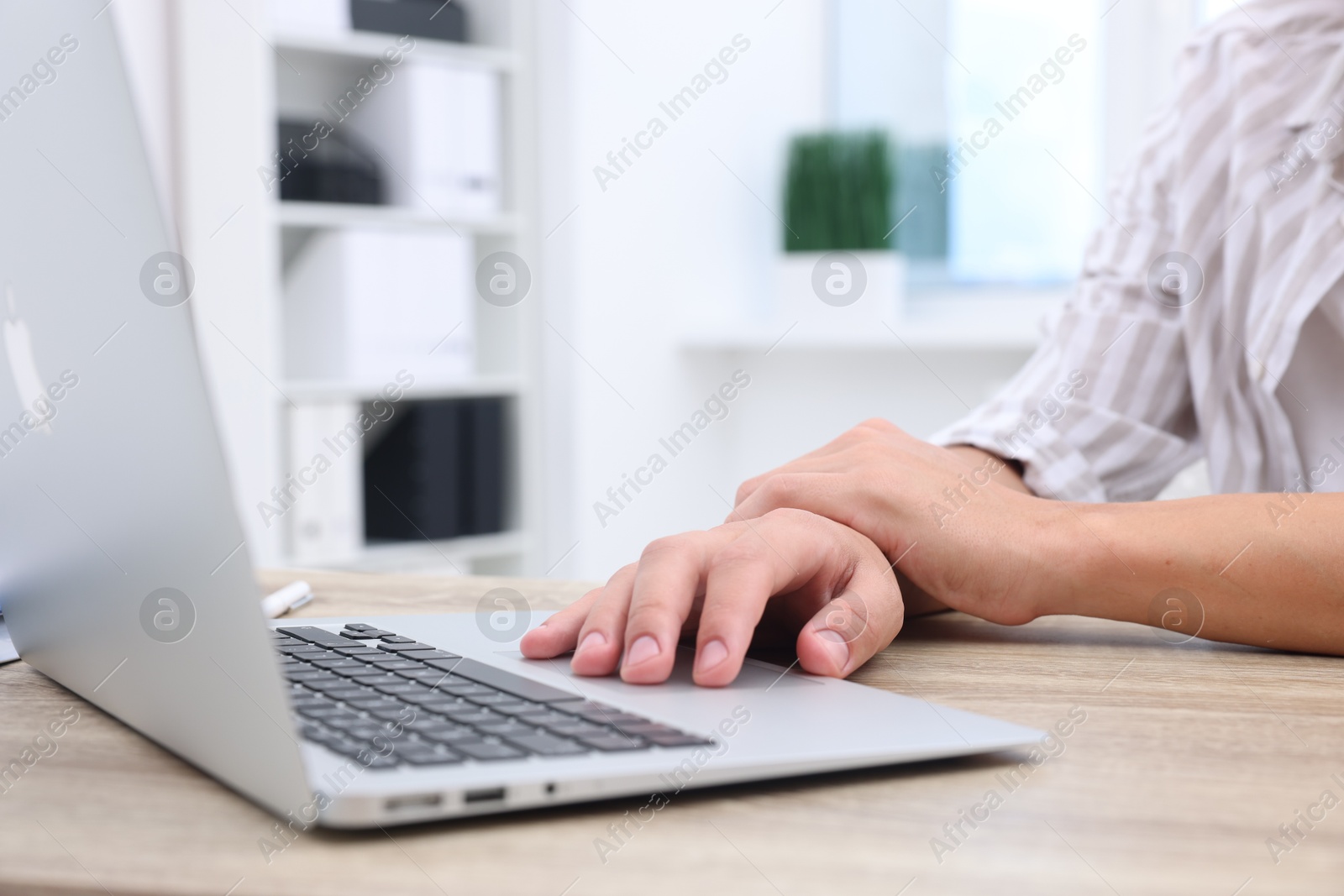 Photo of Man suffering from pain in wrist while working on laptop at table indoors, closeup. Carpal tunnel syndrome