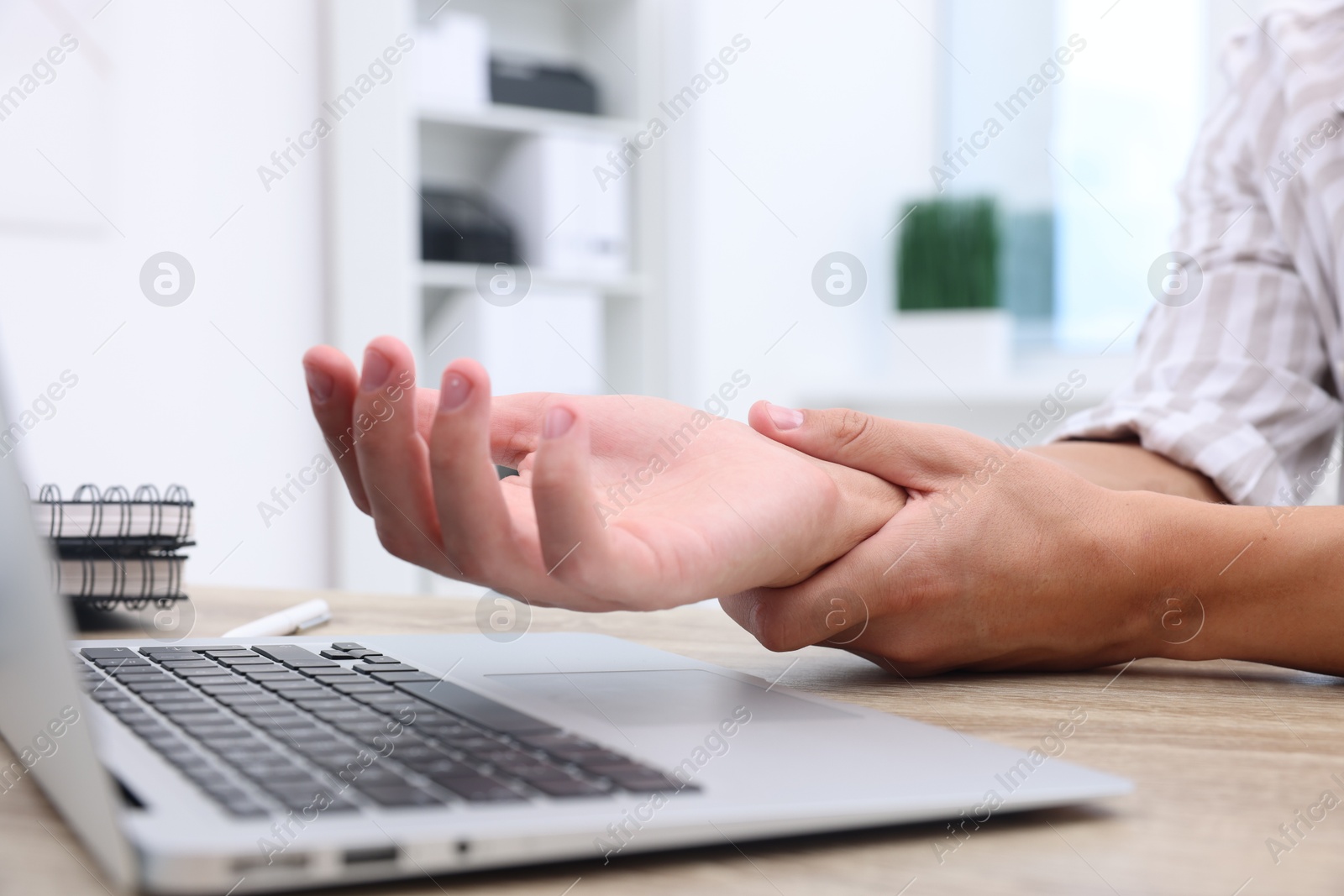 Photo of Man suffering from pain in wrist while working on laptop at table indoors, closeup. Carpal tunnel syndrome